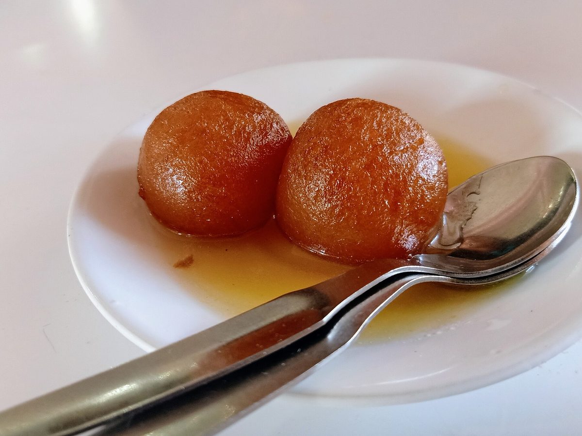 Two gulab jamun in syrup on a white plate