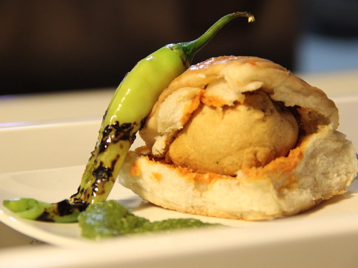 A vada pav with chutney and a fried green chilli